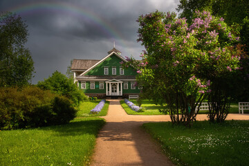 Obraz premium A colorful view of the family nest of the famous Russian poet Pushkin. Summer day. Dark blue sky with rainbow. Wooden house of the Ganibals family. Pushkin mountains. Pskov.