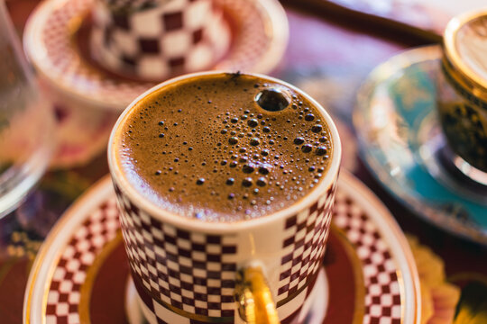 Close-up photo of Turkish coffee with foam in a checkered Turkish coffee or espresso glass on a wooden tray