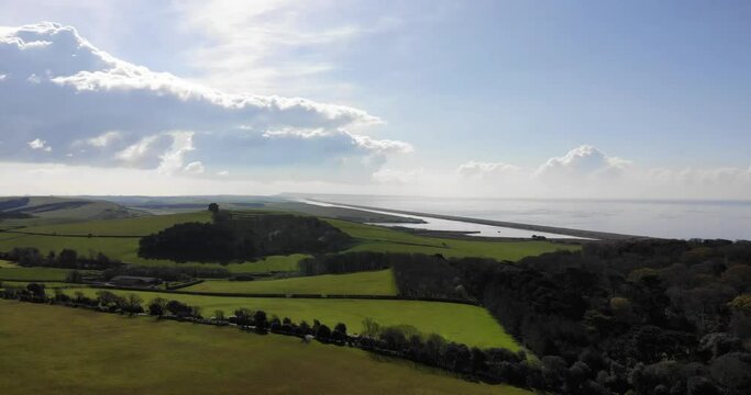 Aerial pull back flying over green fields on the coast next to the ocean in summer