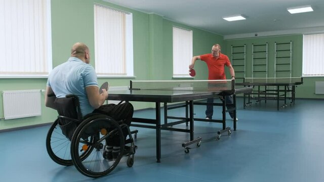 A man in a wheelchair plays ping pong. People with disabilities play table tennis. Rehabilitation of the disabled. Sport.