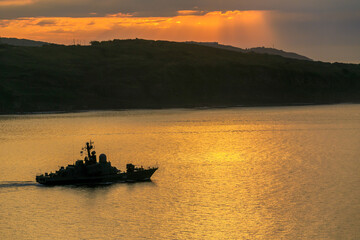 A Russian military ship is sailing during a bright dawn. Silhouette of a Russian military ship in...