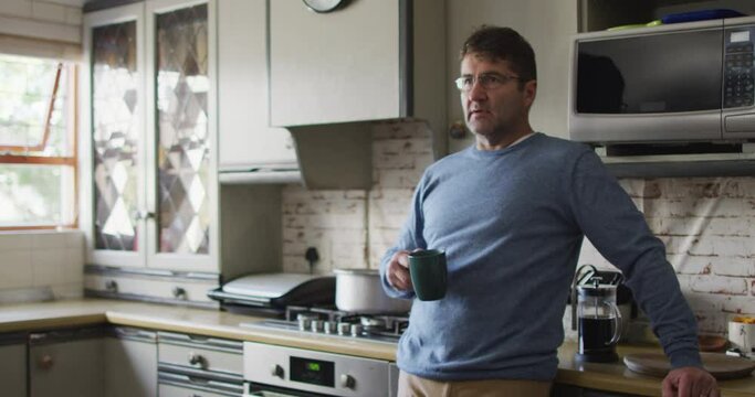 Thoughtful caucasian man drinking coffee in kitchen at home