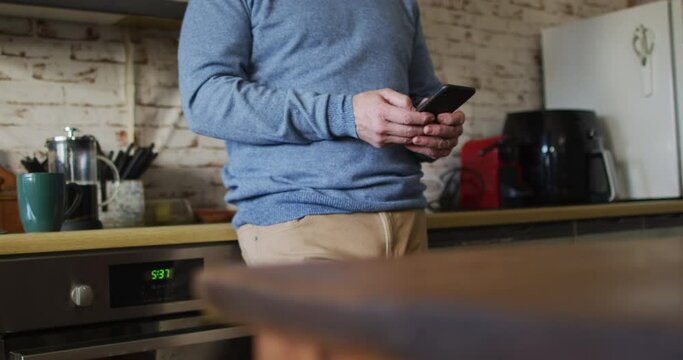 Midsection of caucasian man using smartphone in kitchen at home