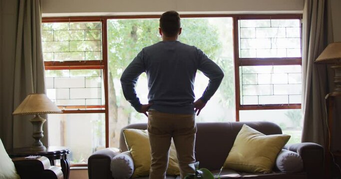 Back view of thoughtful caucasian man standing at window at home