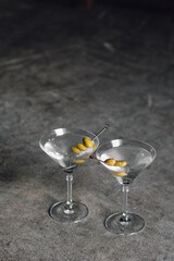 two classic, elegant martini glasses with olives on cocktail picks on gray concrete floor