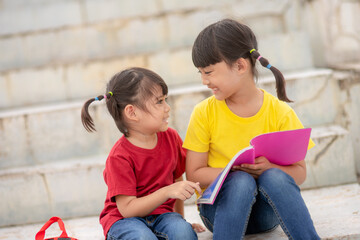 Little Girl and sister reading a book together. Adorable Asian kids enjoying studying outdoors...