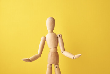 Wooden doll with gesture on yellow background. Mannequin shows gesture. Figure of wooden human with...