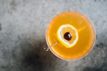 top down shot of a whiskey sour cocktail with lemon and brandied cherry on pick 