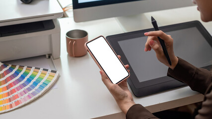 Close-up of the hand woman designer working using smartphone blank white screen tablet color swatches placed at the table.