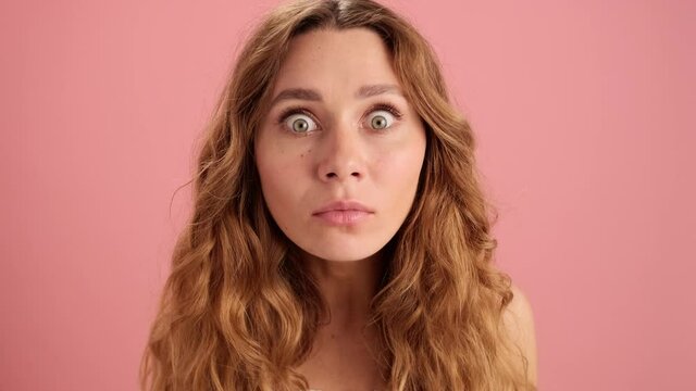 A close-up view of the curly-haired woman looking in surprise at the camera in the orange studio