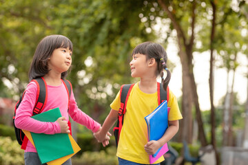 Back to school. Two cute asian child girls with school bag holding book and walk together in the school