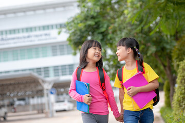 Back to school. Two cute asian child girls with school bag holding book and walk together in the...