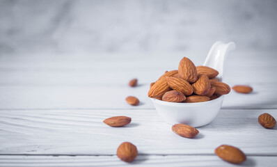 Tasty organic peeled almond snack in white ceramic bowl on white wooden background with copy...