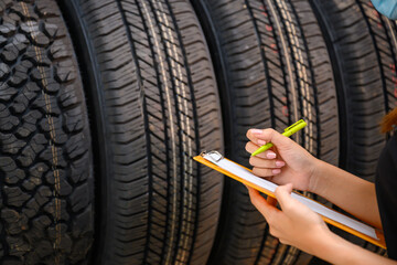 A young woman worker with a clipboard checking stocks of new tires ready to be replaced at a...