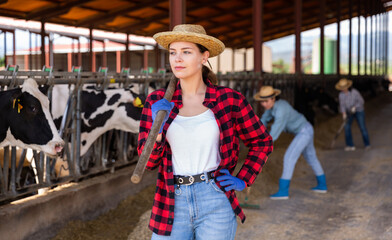 Portrait of confident smiling young woman cow breeder standing in outdoor cowshed on sunny summer day