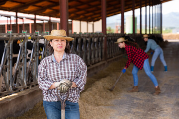 Portrait of mature positive woman farmer working in cowshed at dairy farm