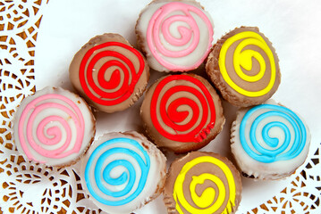 Multi-colored cakes on a white lace napkin. Fresh confectionery close-up. Sweets with sugar icing. 