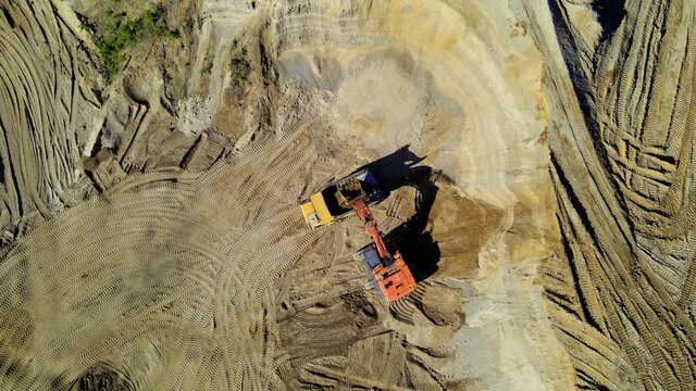 Excavator loading sand into mining truck in open pit. Arial view of heavy mining machinery in quarry. Dump truck transports minerals and limestone from opencast. 