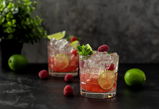 Bourbon or rum raspberry smash cocktail with lime and mint. Refreshing cold drink. dark background, copy space.