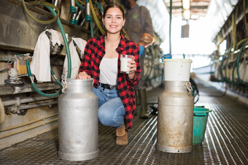 Portrait of young smiling woman professional farmer posing with glass of milk at the cow farm
