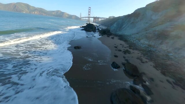 Spectacular drone dive and flight along rocky beach towards Golden Gate Bridge