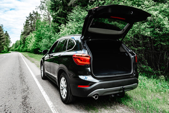 Modern black car with open trunk door on road.