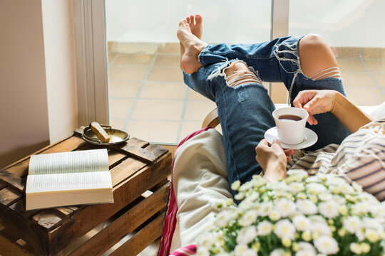 Young woman is relaxing at home, drinking tea, reading book