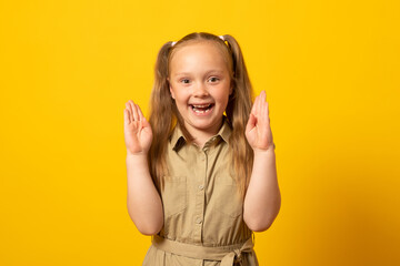 Cute good friendly cheerful girl holding something with her hands while isolated with yellow background.