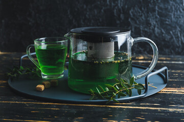 Tea pot and cup of hot green beverage on table