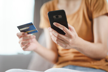 Young woman holding credit card and using smart phone for online shopping, internet banking, e-commerce, spending money, working from home concept