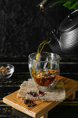 Pouring of hot tea in glass on dark background