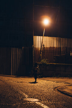 Person In Streetlight Rays Walking Along Street At Night In Suburb