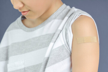 Teenage boy with adhesive bandage plaster on his arm after vaccination. Injection covid vaccine, healthcare for children and teenagers.