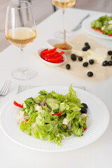 Plates with fresh Greek salad and glasses of wine on table in restaurant