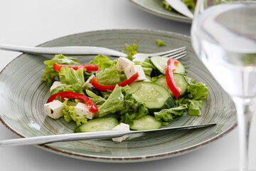 Plate with fresh Greek salad and glass of beverage on table in restaurant