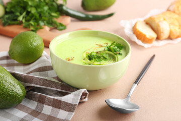 Bowl with green gazpacho and ingredients on color background