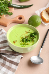 Bowl with green gazpacho and ingredients on color background