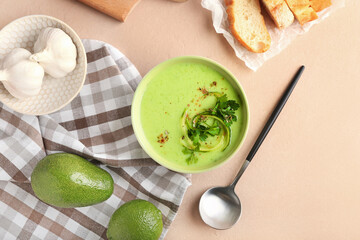 Bowl with green gazpacho and ingredients on color background