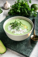 Bowl with green gazpacho and ingredients on grunge background