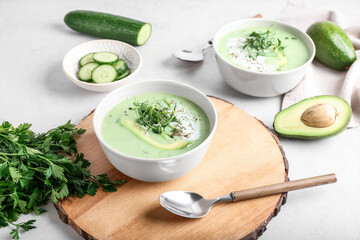 Bowls with green gazpacho and ingredients on light background
