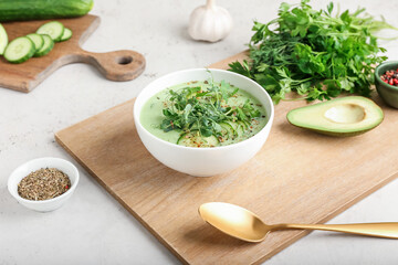 Bowl with green gazpacho and ingredients on light background