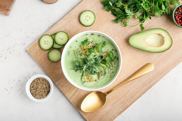 Bowl with green gazpacho and ingredients on light background