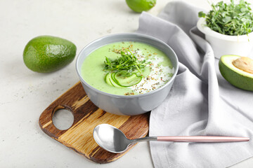 Bowl with green gazpacho and ingredients on light background