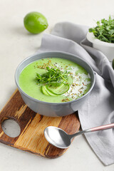 Bowl with green gazpacho and ingredients on light background