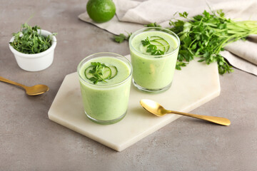 Glasses with green gazpacho, fresh sprouts and parsley on grey background