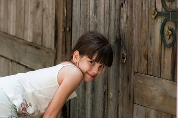 Fototapeta premium The child peeps through a keyhole. The little girl (eight years old) looks through a keyhole of old wooden gate. Outdoors