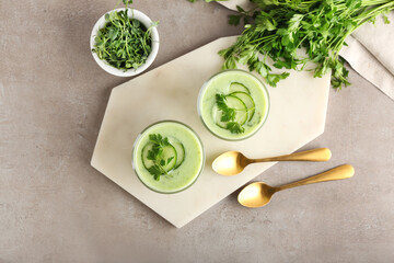 Glasses with green gazpacho, fresh sprouts and parsley on grey background