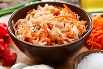 Bowl with tasty sauerkraut and ingredients on wooden background
