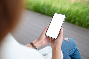 Mockup image of a woman holding mobile phone with blank white desktop screen in the outdoors