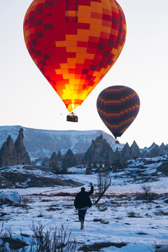 Tourist running toward flying hot air balloons flying up in clou